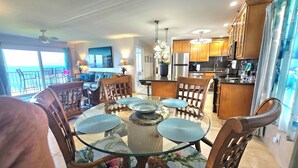 A modern kitchen with wooden cabinets, a stainless steel refrigerator, and a dining area with a glass table and chairs.