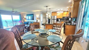 A modern kitchen with wooden cabinets, a stainless steel refrigerator, and a dining area with a glass table and chairs.