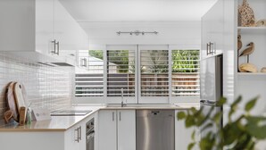 Eine moderne Küche mit weißen Schränken, einem Edelstahl-Geschirrspüler und einem Fenster mit Blick ins Grüne.