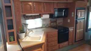 Cocina compacta para autocaravana con armarios de madera, un microondas, una estufa y un lavamanos.