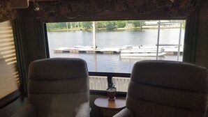 Una cabaña con dos sillones mirando hacia una ventana con vista a un lago con barcos.