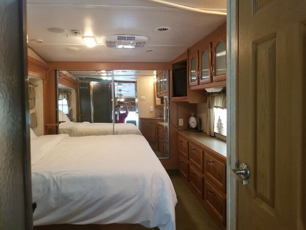 Une chambre avec deux lits, des armoires en bois, une télévision et un miroir.