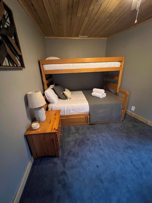 Habitación con literas, cabecero de madera, mesita de noche con lámpara y alfombra azul.