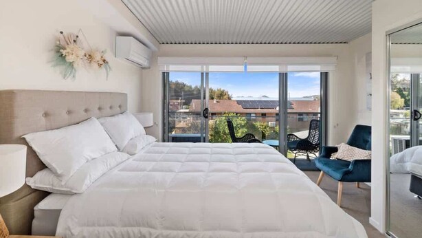 Ein modernes Schlafzimmer mit einem großen Bett, Blick auf die Stadt und einem Balkon mit Stühlen.