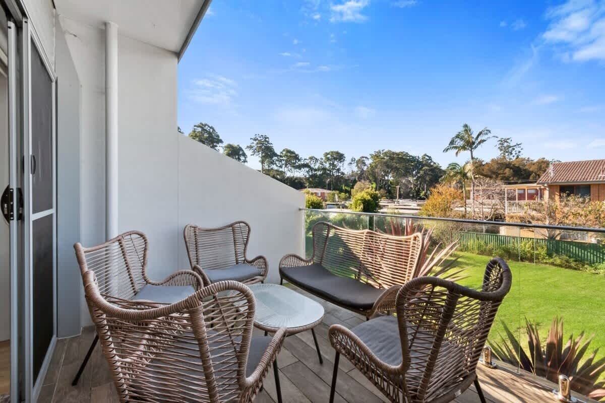 A balcony with wicker furniture, a glass door, and a view of a green lawn and houses.