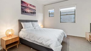 Ein Schlafzimmer mit Bett, Nachttischlampen, einem Nachttisch, einem Gemälde und einem Fenster.