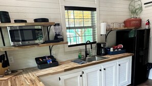 A compact kitchen with a wooden countertop, a microwave, a blender, and a refrigerator.