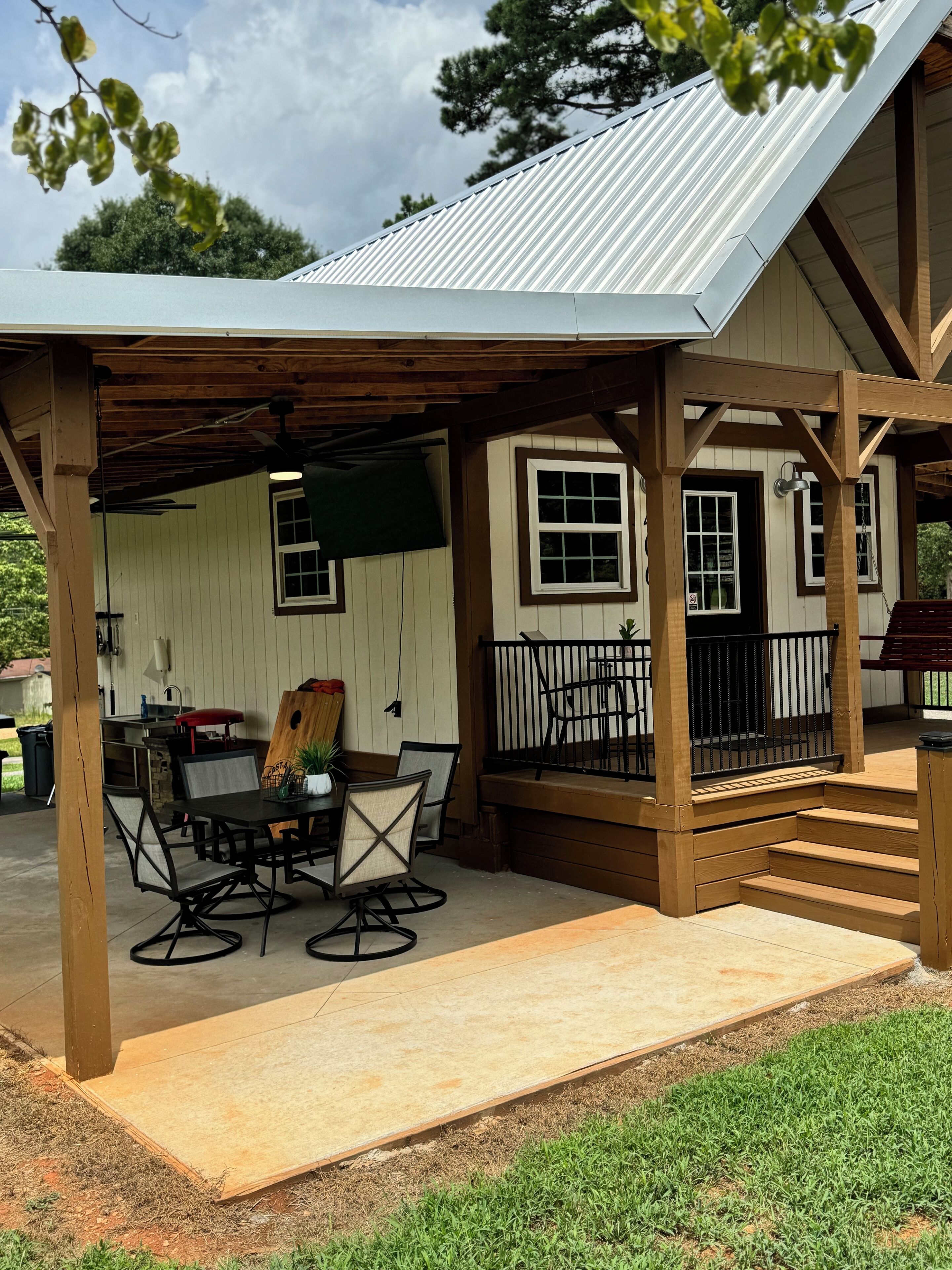 A covered patio area with a table and chairs, a wooden deck, and a metal roof.