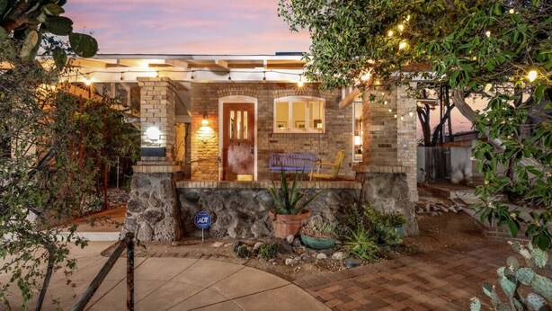 A stone house with a brick entrance, potted plants, and a paved driveway.