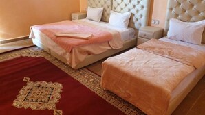 A hotel room with two beds, each with a tufted headboard, a red patterned rug, and a small bedside table. - Sahara Garden (Rissani)