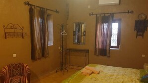 A bedroom with a bed, a chair, a mirror, and curtains. - Sahara Garden (Rissani)