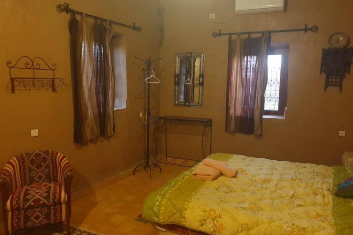 A bedroom with a bed, a chair, a mirror, and curtains.