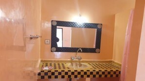A bathroom with a checkered sink, a mirror with a decorative frame, and a door with a towel hanging on it. - Sahara Garden (Rissani)