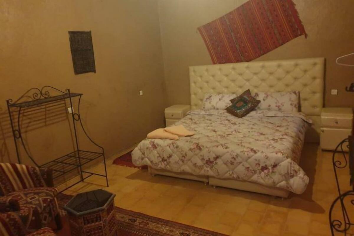 A bedroom with a bed, a small table, a chair, and a hanging tapestry.