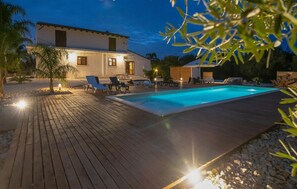 A pool with lounge chairs, a wooden deck, and a building with windows.