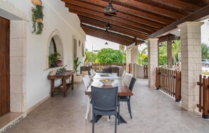 An outdoor patio with a wooden table and chairs, stone pillars, and a view of greenery.