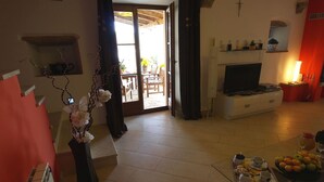 Un soggiorno con televisore, zona pranzo con tavolo e sedie, e angolo cottura con un vassoio di cibo.