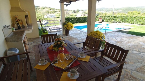 Un tavolo di legno apparecchiato per la colazione con vista su una piscina e colline sullo sfondo.