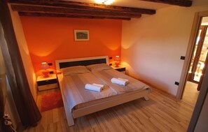 Quarto com cama de madeira, duas mesas de cabeceira, um tapete vermelho e um quadro na parede.