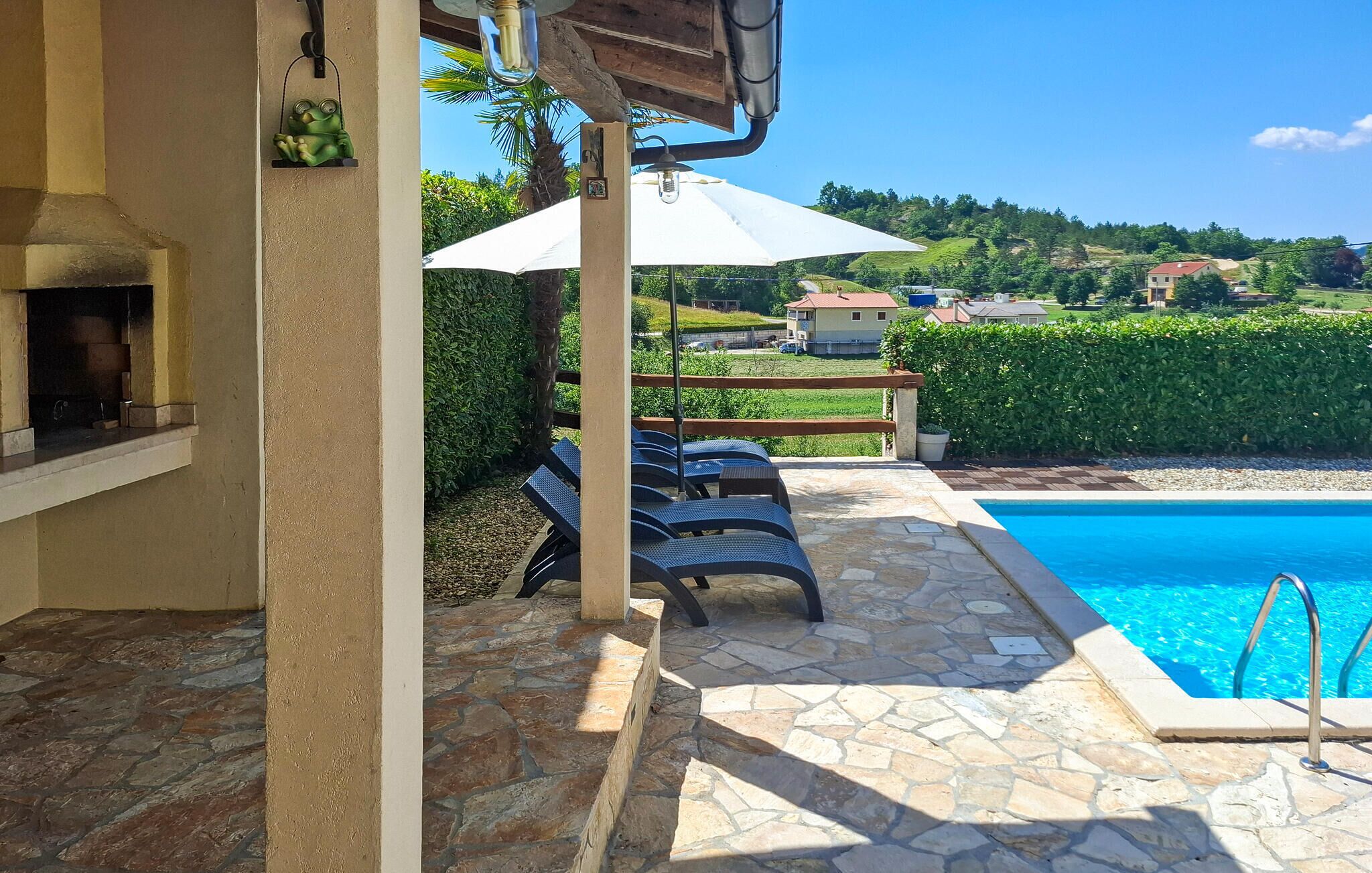 A poolside area with stone flooring, lounge chairs, and a barbecue grill.