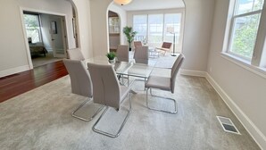 A spacious dining area with a glass table and modern chairs, large windows, and a ceiling light fixture. - Spacious 5 Bedrooms, 7 beds - Sleeps Large Groups (Portland)