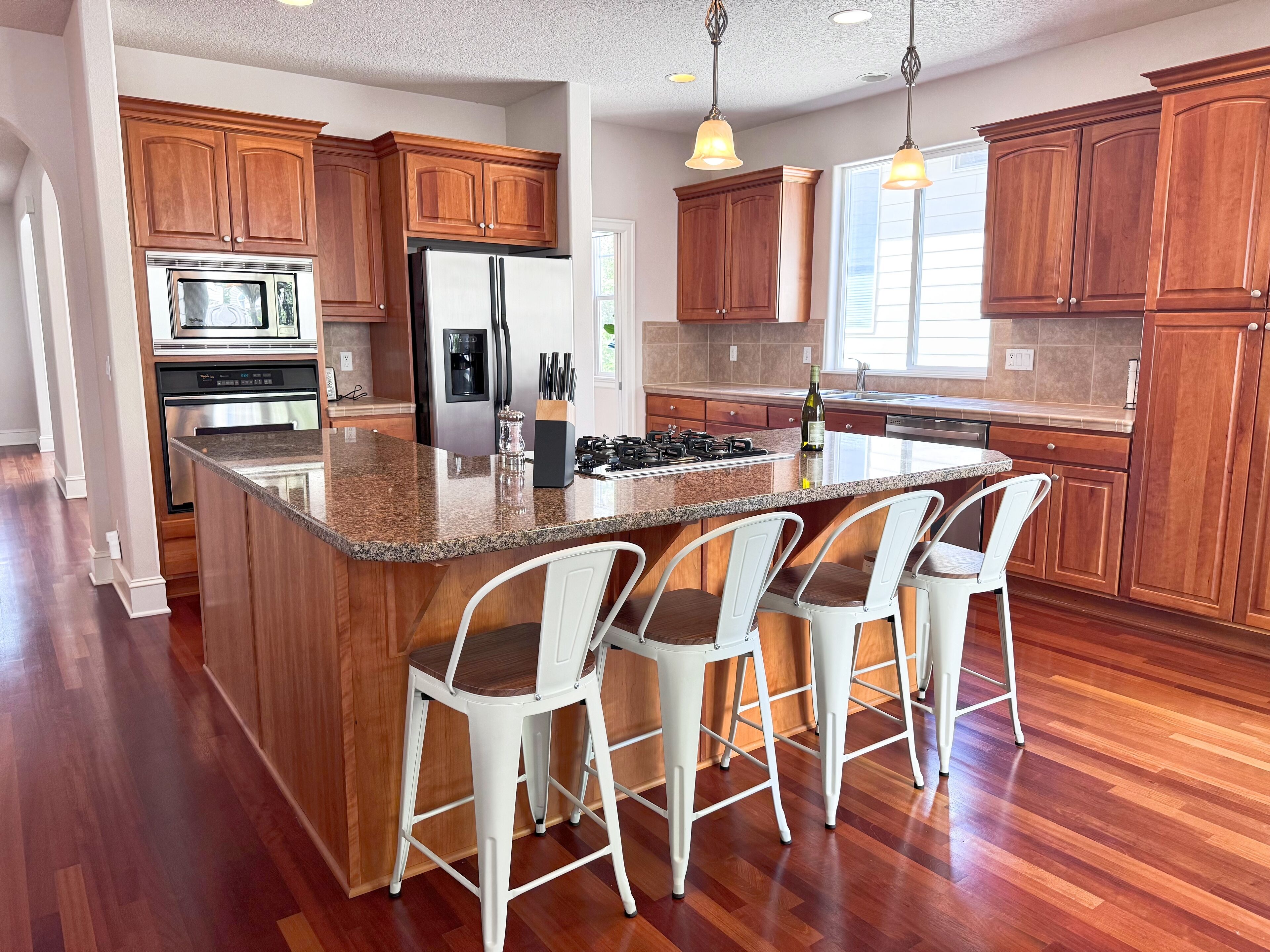 A modern kitchen with wooden cabinets, a granite countertop, and a central island with bar stools.
