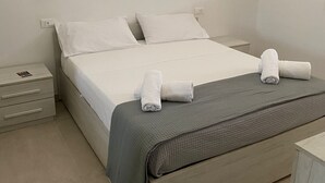 Una cama bien hecha con sábanas blancas y dos toallas enrolladas encima.
