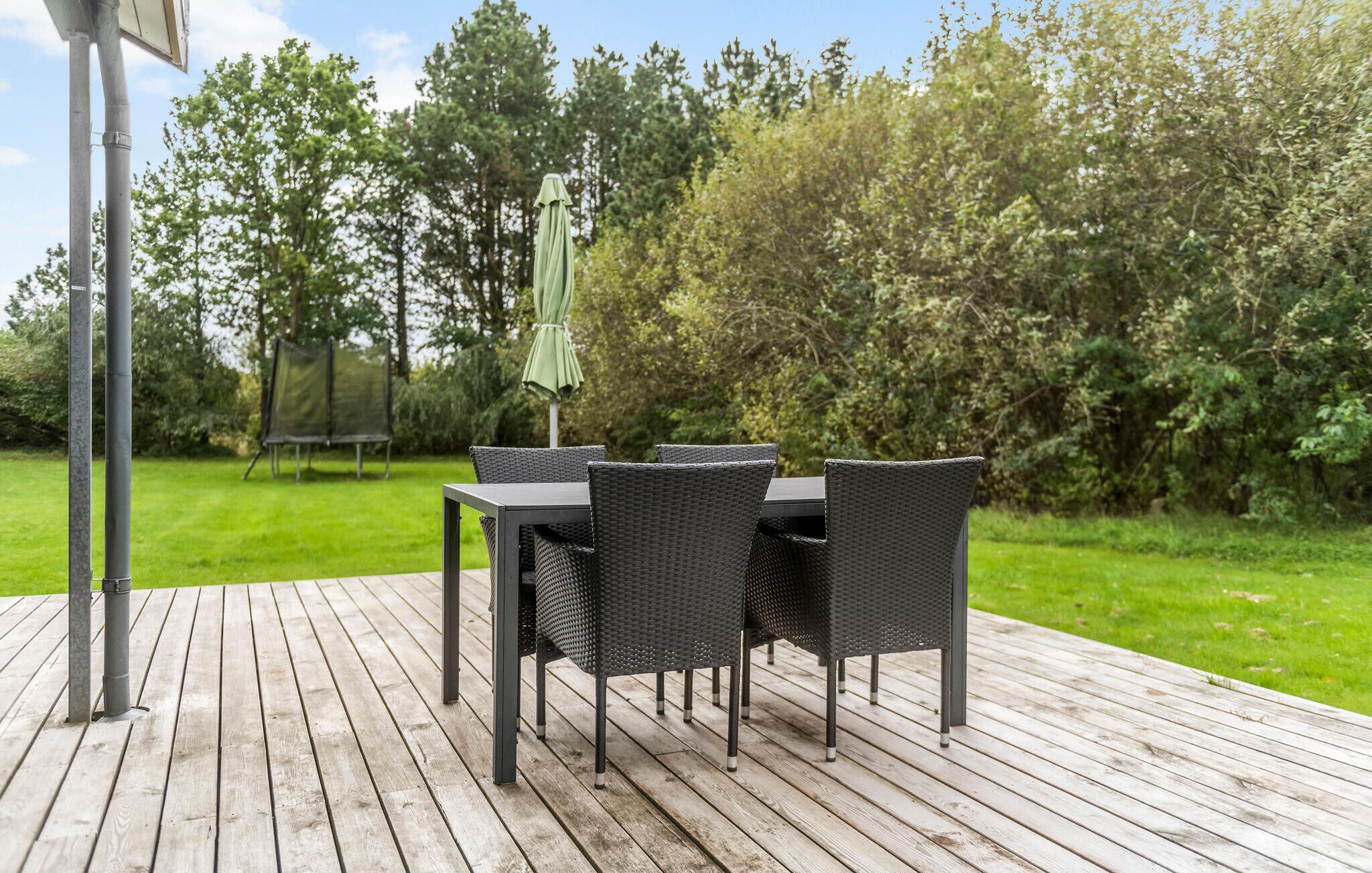 Een houten terras met een tafel en stoelen, omringd door begroeiing.