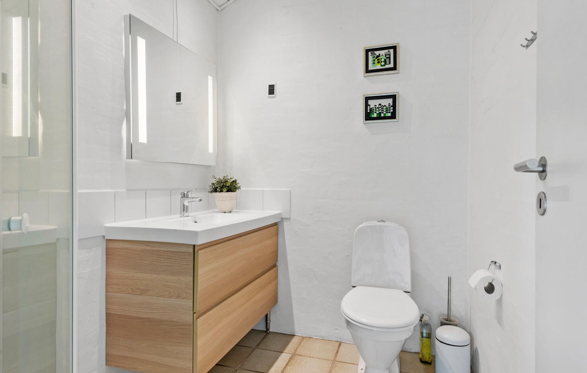 A modern bathroom with a white sink, wooden vanity, a toilet, and a glass shower enclosure.