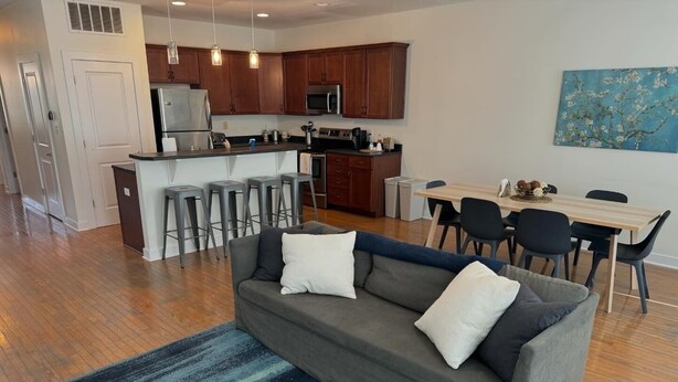 A modern apartment with a grey sofa, a dining table, and a kitchen area. - Spacious 3BR 3BA above Brewery, Pizza Shop & Arcade 5 mins to DT Indy (Indianapolis)