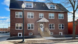 A two-story brick building with a number '104' displayed above the entrance. - 2 Bedroom Apartment - Downtown (Marshall)