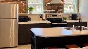 A modern kitchen with a brick wall, stainless steel appliances, a central island with a sink, and pendant lighting. - 2 Bedroom Apartment - Downtown (Marshall)