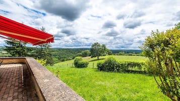 A patio with a red-striped awning, a brick ledge, and a view of a green landscape with trees and rolling hills.