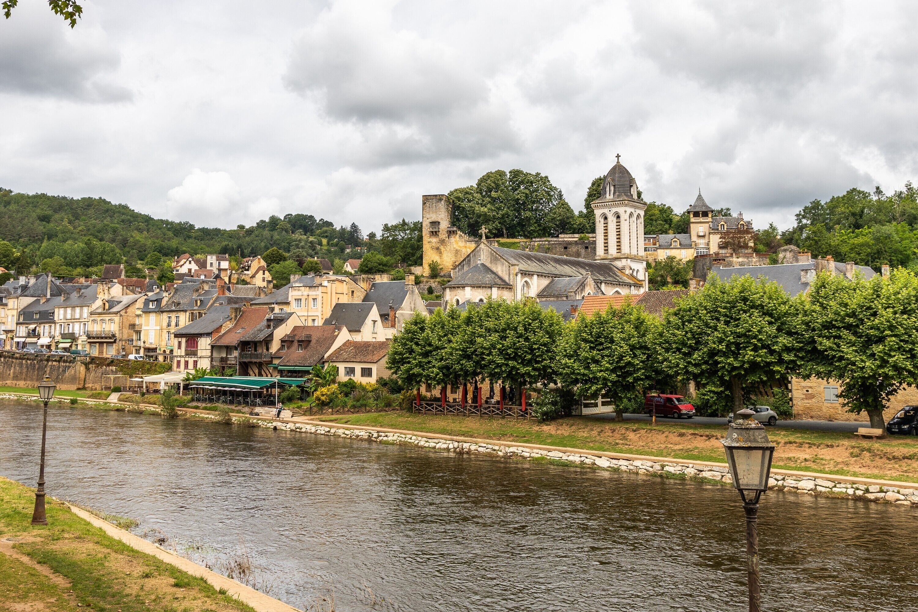 A riverside town with historic buildings, a prominent church tower, and a paved walkway along the water.