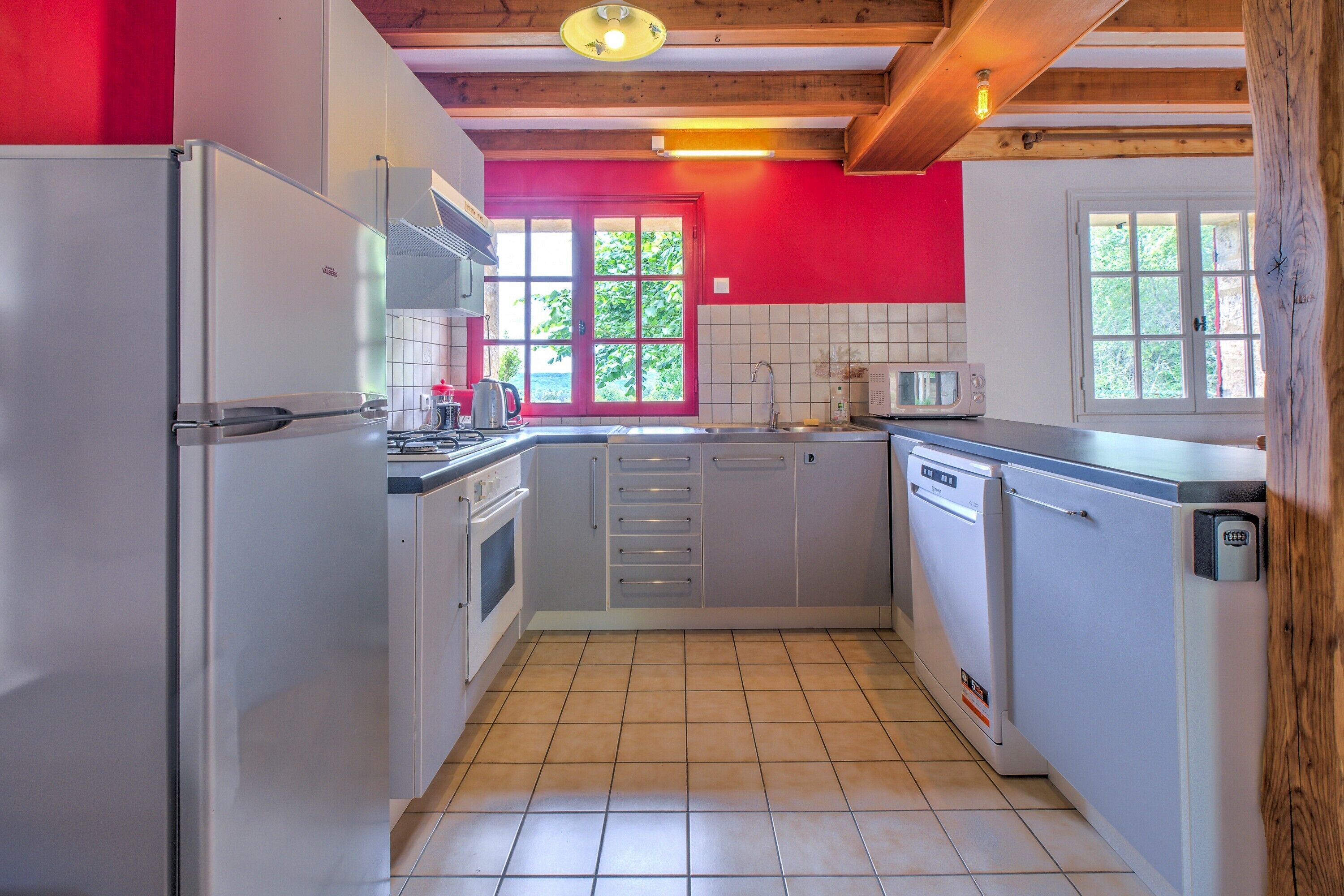 A compact kitchen with white appliances, a red accent wall, and a window providing natural light.
