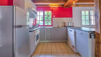 A compact kitchen with white appliances, a red accent wall, and a window providing natural light.