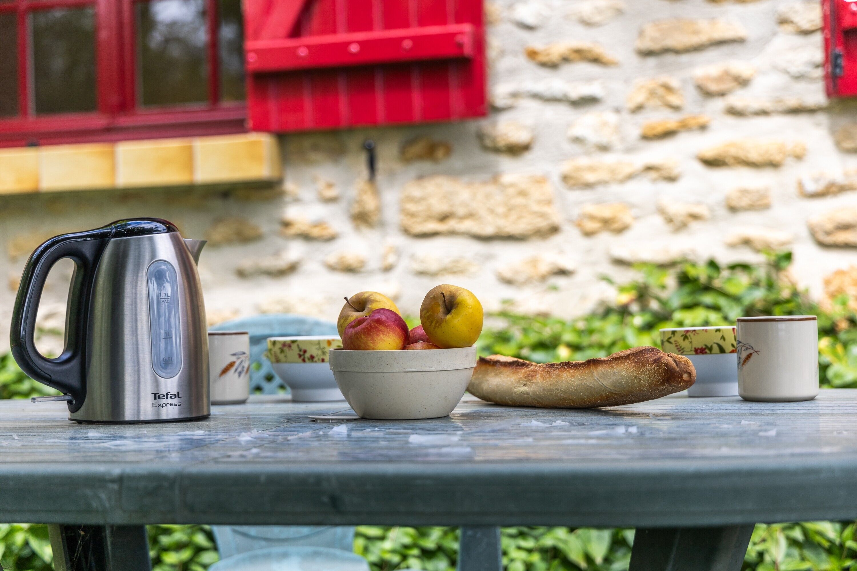 A table with a kettle, a bowl of fruit, a baguette, and cups.
