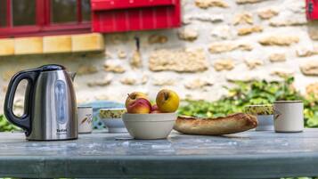 A table with a kettle, a bowl of fruit, a baguette, and cups.