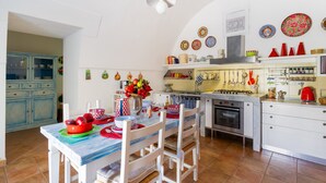 A kitchen with white cabinets, a dining table with chairs, a stove, and various kitchen utensils.