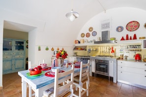A kitchen with white cabinets, a dining table with chairs, a stove, and various kitchen utensils.