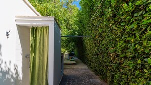 A narrow stone pathway leading to a white building with a green curtain, surrounded by dense green foliage.