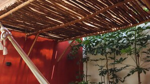 A hammock over a stone-tiled area with a hot tub, surrounded by potted plants and a red wall.