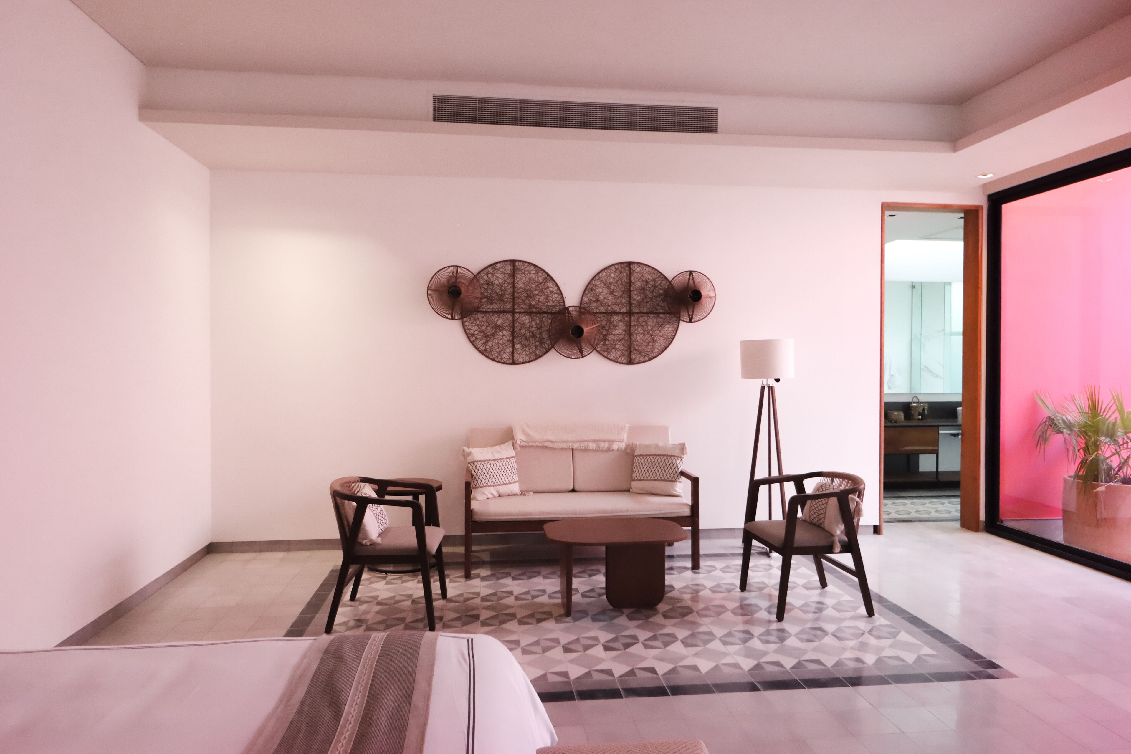 A modern living room with a sofa, two armchairs, a coffee table, and a floor lamp. There is a patterned rug on the floor, and a large mirror on the wall.