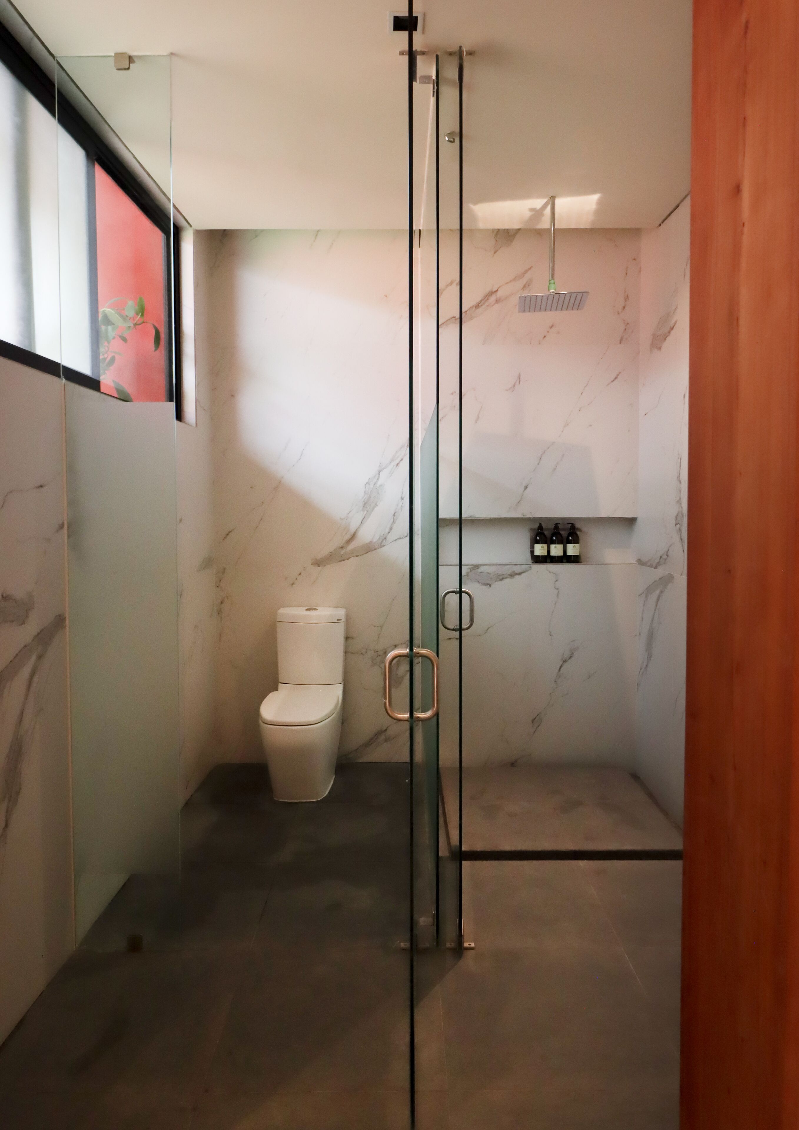 Un bagno moderno con cabina doccia in vetro, un water e pareti in marmo.