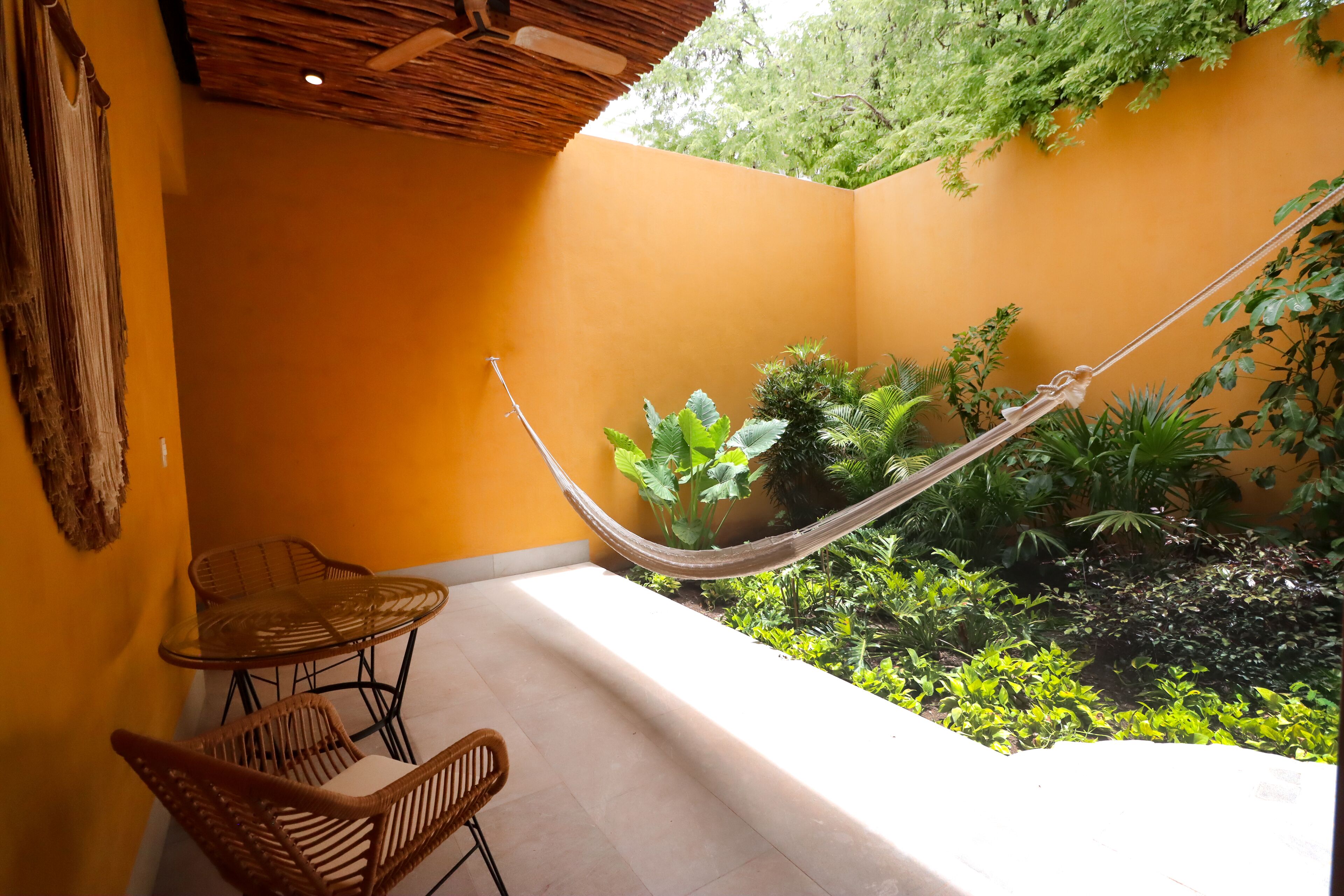 Un petit espace extérieur aménagé avec un hamac, des fauteuils en osier et diverses plantes.