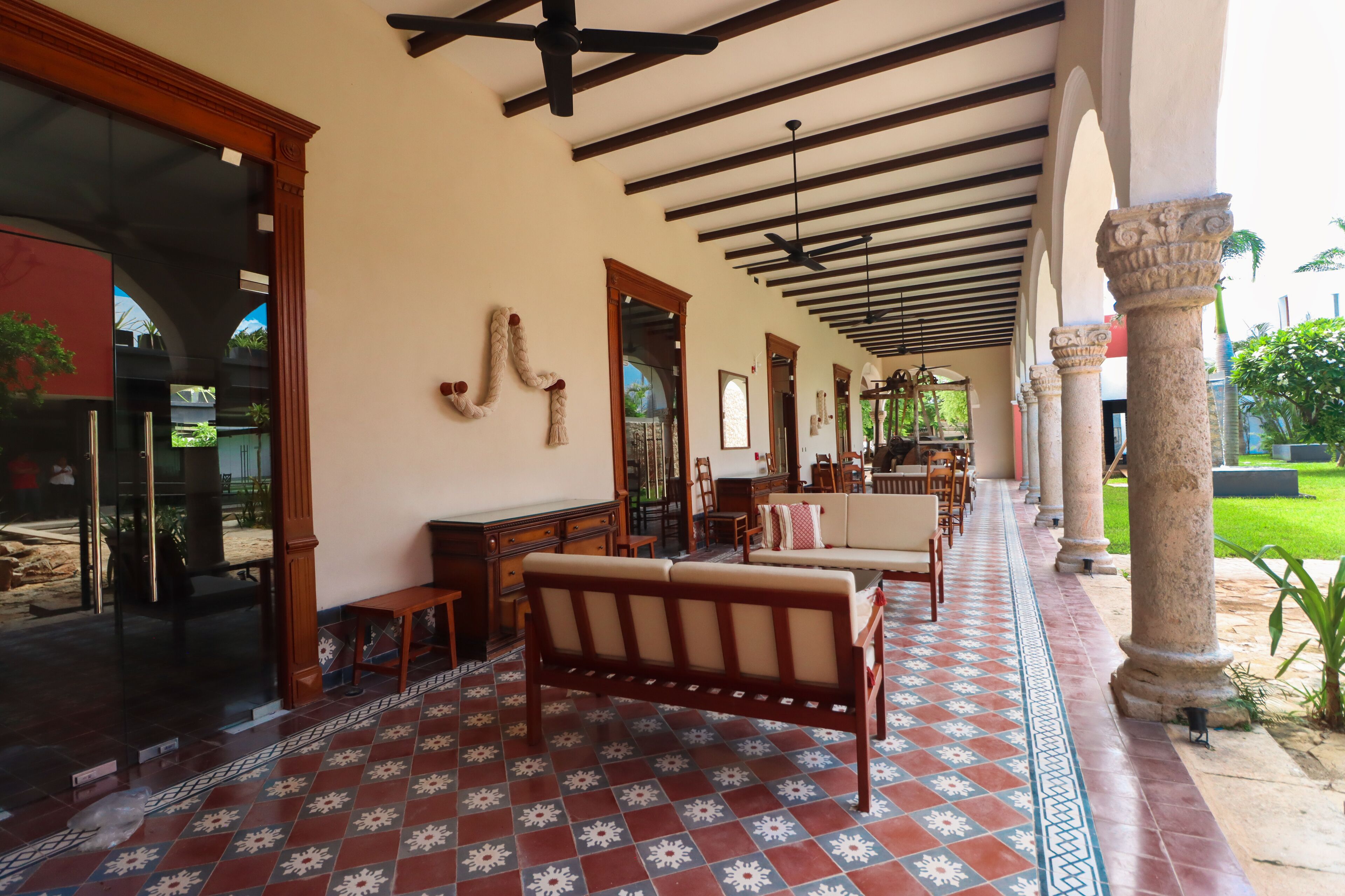 A covered outdoor area with a tiled floor, wooden furniture, and stone columns.