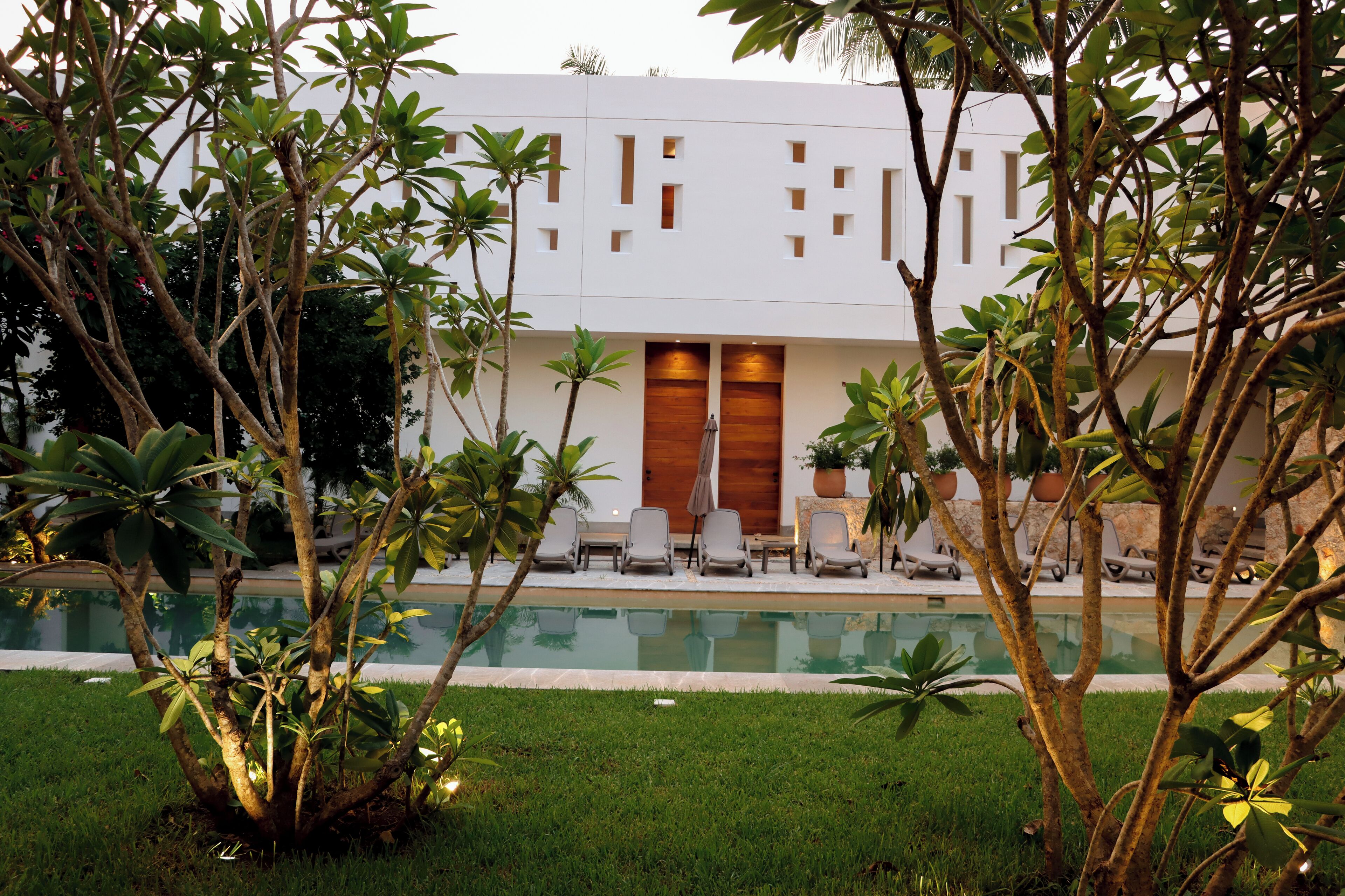 A modern building with a pool, surrounded by lush greenery and outdoor seating.