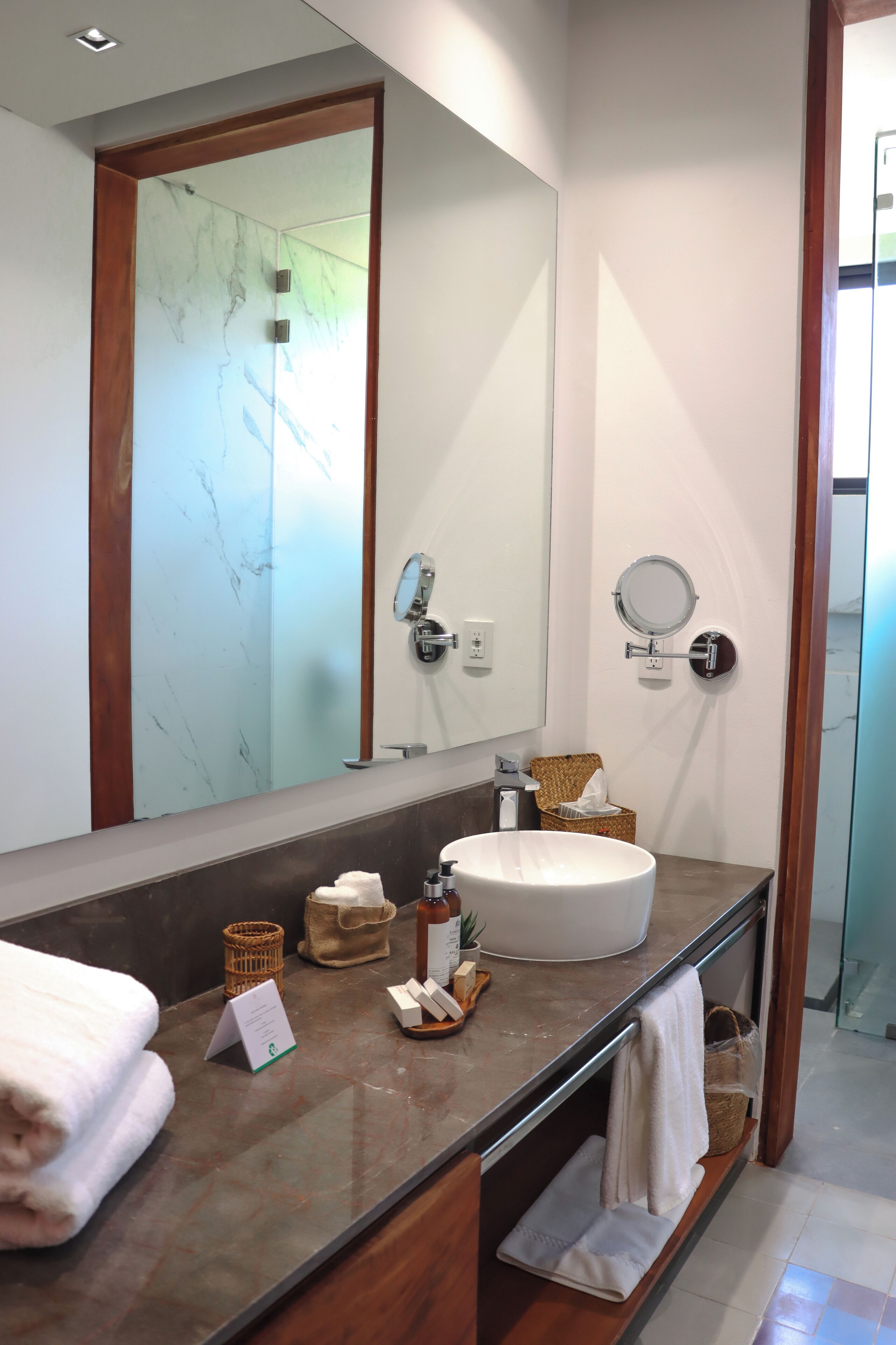 A modern bathroom with a large mirror, a round wall mirror, a sink, and a towel rack.