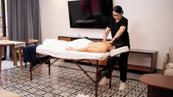 A massage therapy room with a massage table, a TV, and a patterned floor.