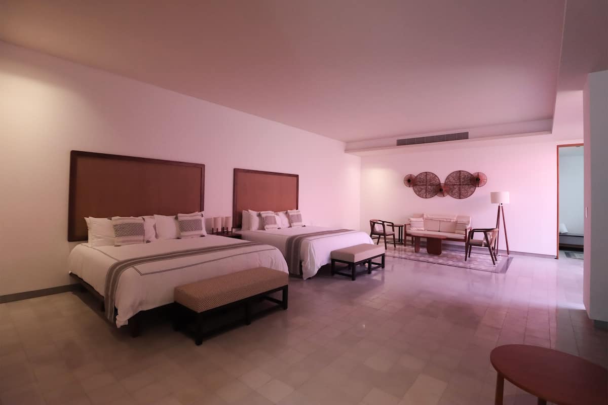 Habitación de hotel con dos camas, un sofá, una silla y una mesita.